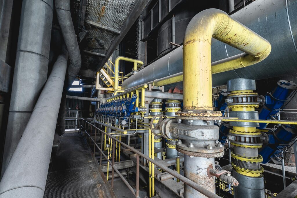 Close-up of an intricate industrial pipeline system featuring yellow valves and steel structures inside a factory.